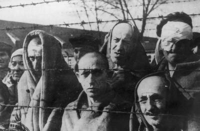 syg. GK-9-1-50-2, Zbliżenie grupy ocalałych więźniów stojacych za drutami obozu koncentracyjnego KL Auschwitz-Birkenau. Autor nieznany. Domena publiczna. Źródło AIPN.