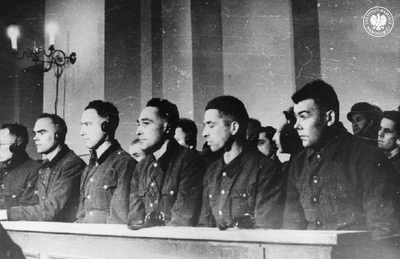 Członkowie załogi obozu KL Plaszow podczas procesu przed Sądem Okręgowym w Krakowie. W pierwszym rzędzie od prawej siedzą: były komendant obozu Arnold Büscher, Edmund Zdrojewski, Lorenz Landstorfer, Ferdinand Glaser, F.W. Korthals, Andreas Dreer. Wszyscy w wojskowych kurtkach mundurowych pozbawionych oznaczeń i dystynkcji oraz w słuchawkach na uszach. Kraków, 8 stycznia 1948 r. Źródło: CAF (fot. z zasobu AIPN)